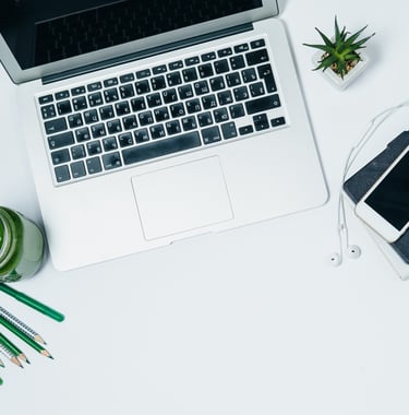 a laptop computer and a phone on a desk with a green plant, pencils and smoothie