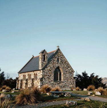 A serene shot of the historic stone Church of the Good Shepherd at Lake Tekapo, Oceania / New Zealand, under a clear blue sky. Professional composition emphasizing a peaceful, stress-free travel atmosphere in soft white and pale blue tones.