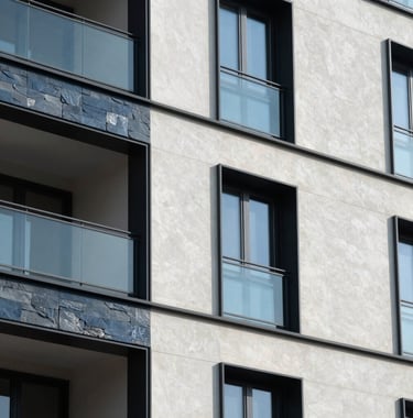 A close-up shot of architectural details on a modern residential building, showing a mix of glass and dark slate blue panels against a soft off-white wall.