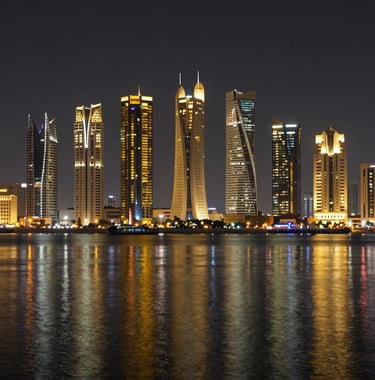 A nighttime photograph of the financial district in Manama, Bahrain, with shimmering gold and white lights reflected on the water, representing global commerce.