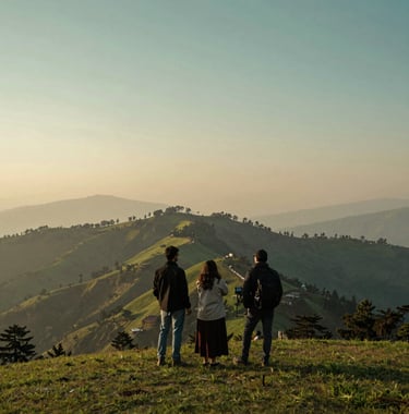 Travelers enjoying a scenic view of the Shimla ridge at sunset, golden hour lighting, soft sage green and teal colors in the landscape, South Asian / Indian scenery.