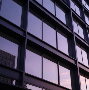 An artistic shot of modern corporate architecture in the US, showing clean lines and deep navy steel beams reflecting a soft purple sunset. Symbolic of strength and scale.