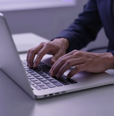 A close-up, high-end photograph of a professional's hands working on a sleek, thin laptop in a minimalist, modern office in North America. The lighting is cool-toned with soft purple accents, focusing on clean design and a sense of focused technological innovation.