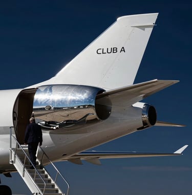 A close-up shot of a polished silver luxury jet tail against a clear dark navy blue sky, with a Global / Sophisticated Traveler walking towards the stairs. High-contrast professional photography.
