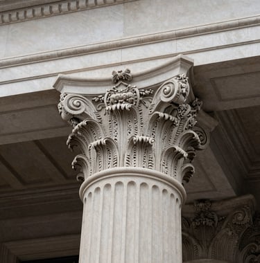 An architectural close-up of a classic Corinthian column capital on a historic North American / US library building. The image conveys strength and stability, captured in sharp detail with a Pearl Mist color palette.