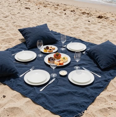 An overhead shot of a perfectly arranged luxury picnic on a secluded beach. Muted navy blue textiles, white ceramics, and gourmet snacks. The lighting is bright and airy, reflecting a stress-free luxury vacation vibe.