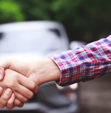 two people shaking hands with a car in the background