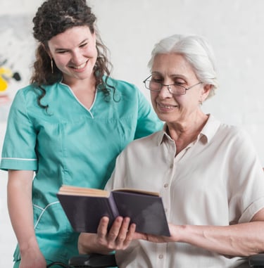 a senior woman reading a book with her caregiver