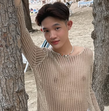 Young mad stood between 2 trees wearing a cream coloured mesh long sleeve top