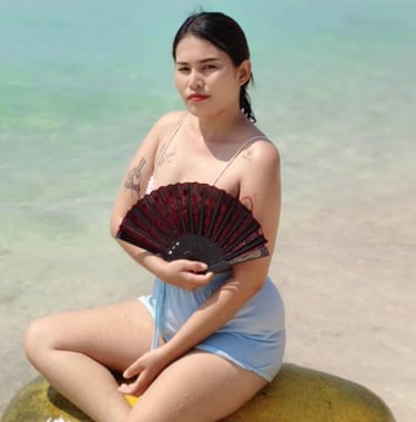 Lady sitting on a float at the beach and holding a fan in her hand