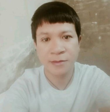 Man wearing a light shirt, looking at the camera indoors with a calm expression and soft lighting.