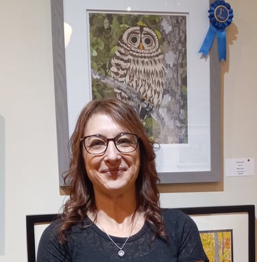 Artist smiling in front of her first-place award-winning owl mosaic artwork at an art gallery.