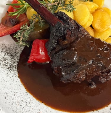 Braised lamb shank with rich red wine sauce, roasted potatoes, and fresh rosemary garnish.