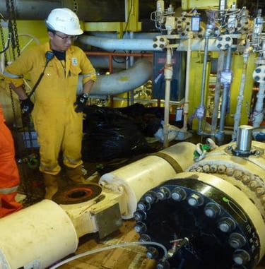 Oil and gas engineers in coveralls inspecting industrial pipeline valves on an offshore platform.