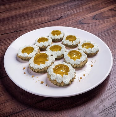 Mini fruit tarts with whipped cream swirls and apricot glaze on a white plate over a dark wood table.