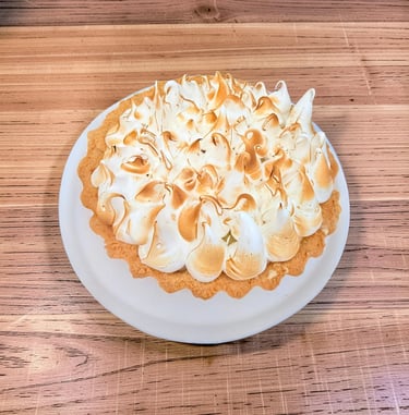 Homemade lemon meringue tart with toasted peaks on a white plate over a wooden table.