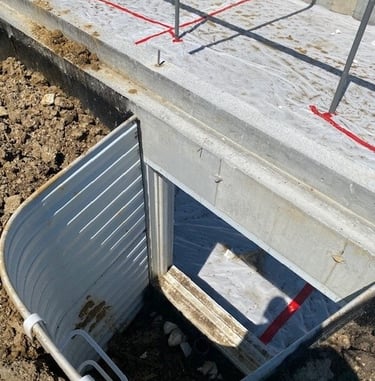 Egress window well installed against a concrete foundation on a construction site.