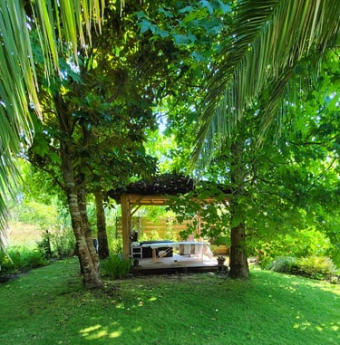 Table de massage installée sous un gazebo balinais en bois au mileu d'un jardin luxuriant