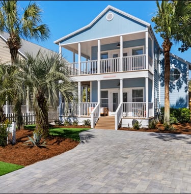 Luxury blue two-story beach house rental with a paved driveway and palm trees.