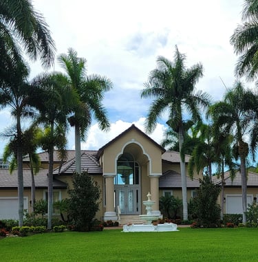 Luxury Florida mansion featuring palm tree landscaping, a green lawn, and a white tiered water fountain.
