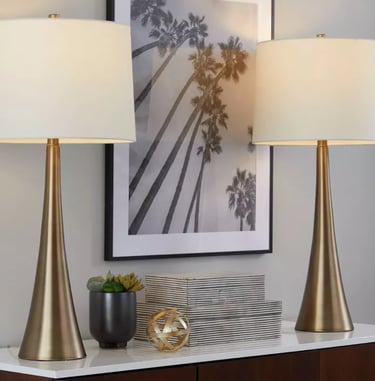 Pair of mid-century modern gold table lamps with white drum shades on a console table.