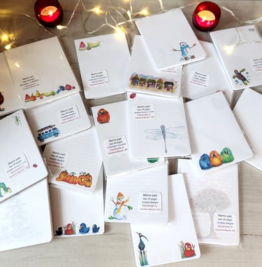 Handmade tear-off memo pads with colorful illustrations, pumpkins, and birds on a wooden table.
