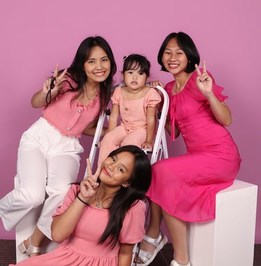 Three young ladies and a small girl in pink dresses on pink background