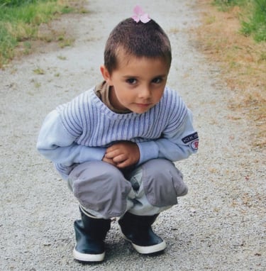 a young boy is sitting on a gravel road