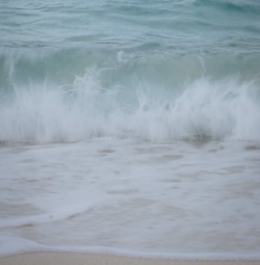 Slow shutter image of waves crashing on beach, pastel blues.