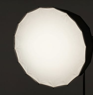 A side view of a large studio softbox diffusing light in a dark, minimalist space. The atmosphere is professional and quiet, reflecting a North American artistic workshop aesthetic. Colors are restricted to black, dark gray, and off-white.