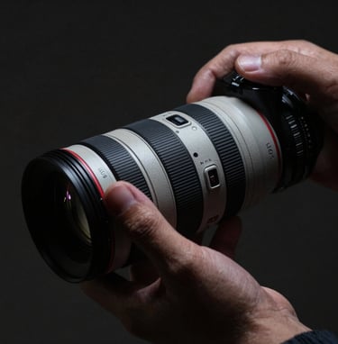 Close-up of a photographer's hand adjusting a high-end lens in a dimly lit North American studio. The lighting is dramatic and moody, with deep shadows and soft highlights of light gray on metallic surfaces.
