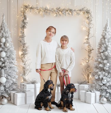 Mother and daughter posing with two spaniel dogs in a white winter holiday studio setting with lights.