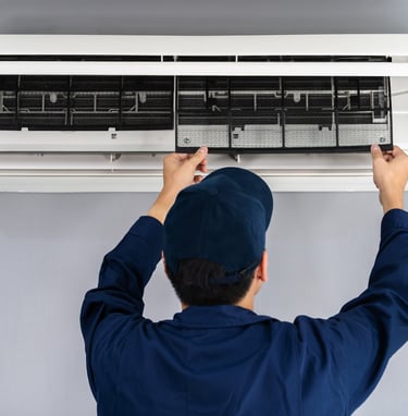 A technician servicing an air conditioner, removing the air filter for cleaning and maintenance purposes.