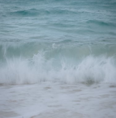 Slow shutter image of waves crashing on beach, pastel blues.