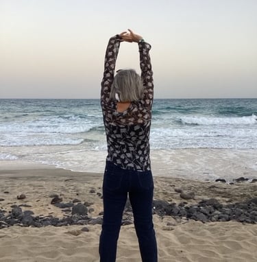 a woman standing on a beach with her arms up in the air