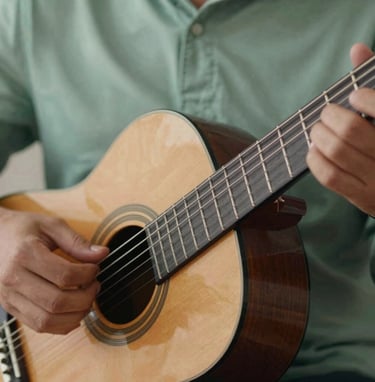 A close-up shot of Lyan Galindo's hands gracefully playing a classical guitar. The lighting is intimate and warm, emphasizing the texture of the strings and the motion. Incorporates #91AA9D sage tones in the background fabric for a sophisticated, calming feel.