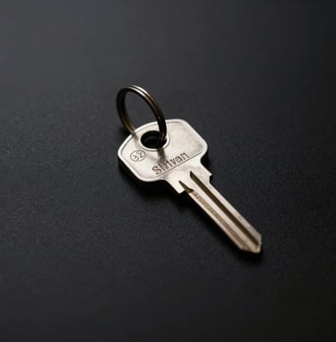 A minimalist square photograph of a single silver key on a clean black surface, symbolizing private access. Muted brown and gray tones, modern and refined Spanish aesthetic.