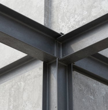 An architectural detail shot focusing on the intersection of steel and concrete. The lighting is clean and professional, highlighting the textures of #6B6760 metal and the smooth #FBF9F6 concrete surfaces. Modern and precise composition.