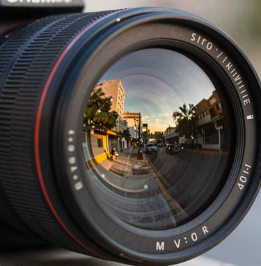 Close up shot of a professional camera lens reflecting a blurred, vibrant Latin American / Hispanic urban scene at golden hour, sophisticated and sharp.