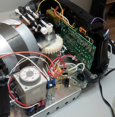 Internal view of a machine showing a timer relay, circuit board, gears, and electrical wiring for repair.