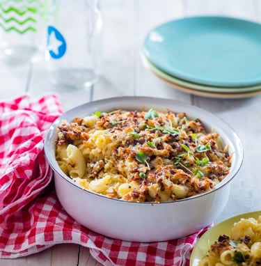 Mac n Cheese with a crunchy topping in an enamel bowl with serving plates to the rear and a napkin