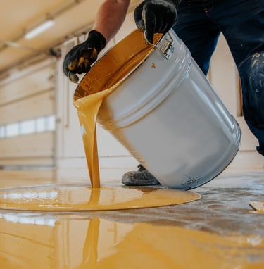 a man is pouring a bucket of paint onto a floor