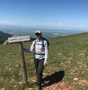 a woman in a hat and backpack standing on a mountain