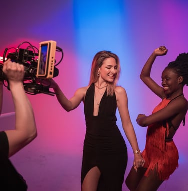 Two women stand in front of a studio camera dancing 