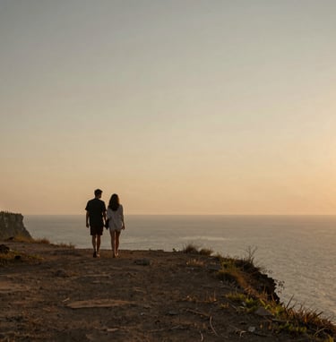 A cinematic shot of a couple walking along a quiet Uluwatu cliff at sunset. Golden hour lighting casting long shadows, minimalist horizon, featuring earthy tones of #7B6654 and #C8B6A6.