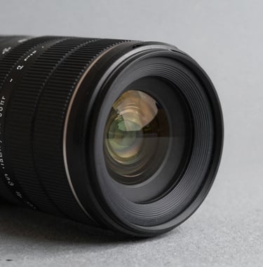 Detail shot of a professional camera lens on a soft gray surface, sharp focus, minimal composition, charcoal black accents, Global / Contemporary Art.