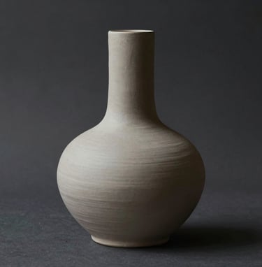 A minimalist ceramic sculpture with organic, fluid lines. The piece is a soft #C8C0B2 color, set against a deep #1A1A1A shadow. The lighting is focused and contemplative, highlighting the physical texture of the clay.