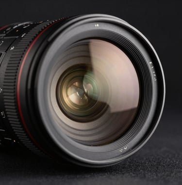 A close-up photograph of a professional camera lens reflecting a soft, warm cream glow, set against a deep charcoal black background. The style is sharp, clean, and luxurious, representative of a North American / European professional studio.