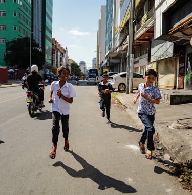 Childrens running down a street during a sunny day in Phnom Penh, Cambodia - by ACAT PHOTOS