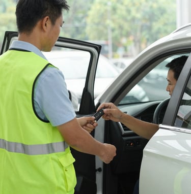 A smiling valet opening the car door for a guest arriving at an elegant event entrance.